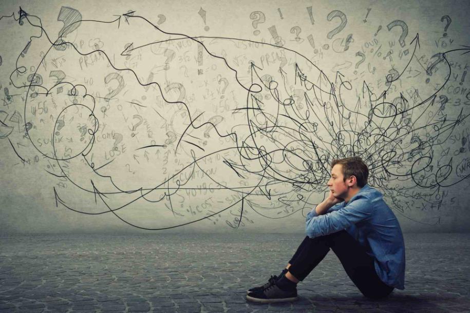 Young man sitting alone with chaotic drawings behind him representing overthinking and anxiety