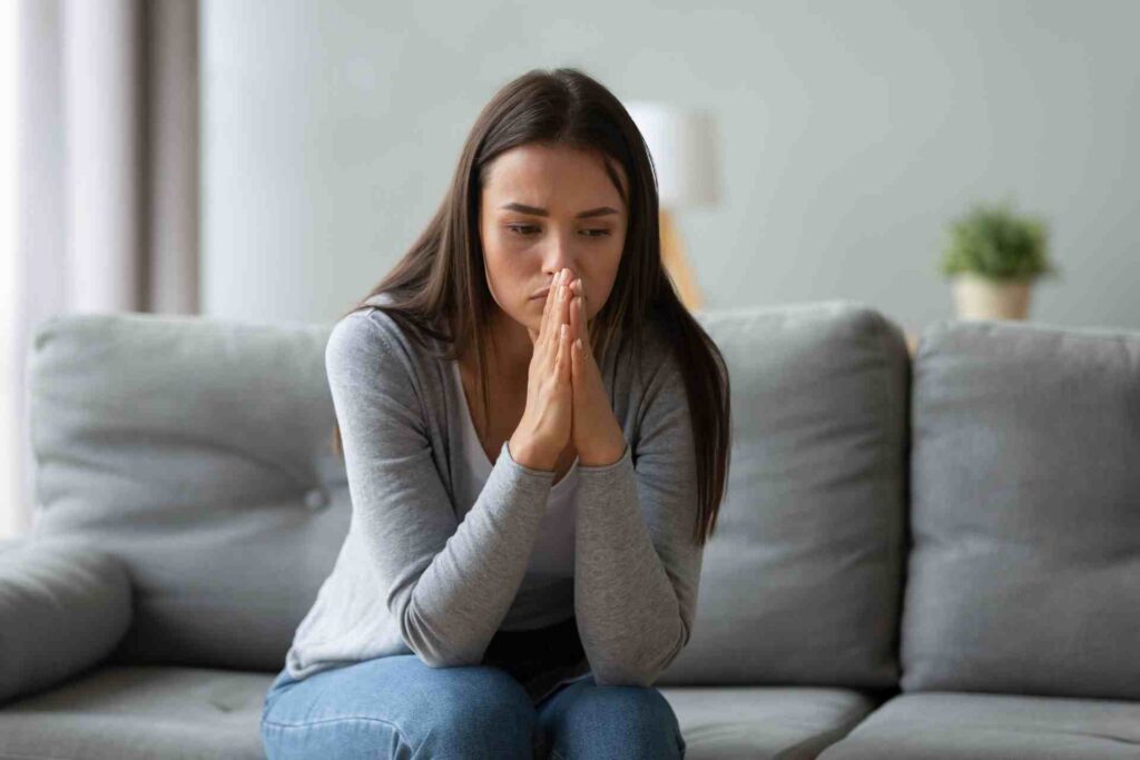 Young woman sitting on a couch appearing worried and overwhelmed by anxiety