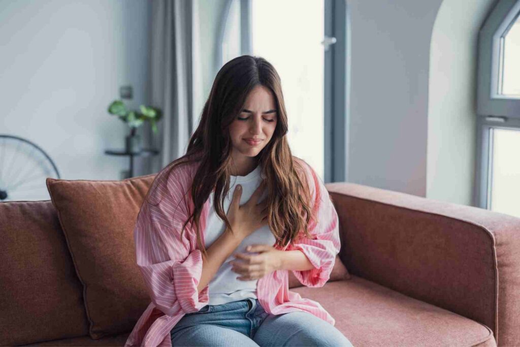 Woman holding her chest while experiencing anxiety-related chest pain at home