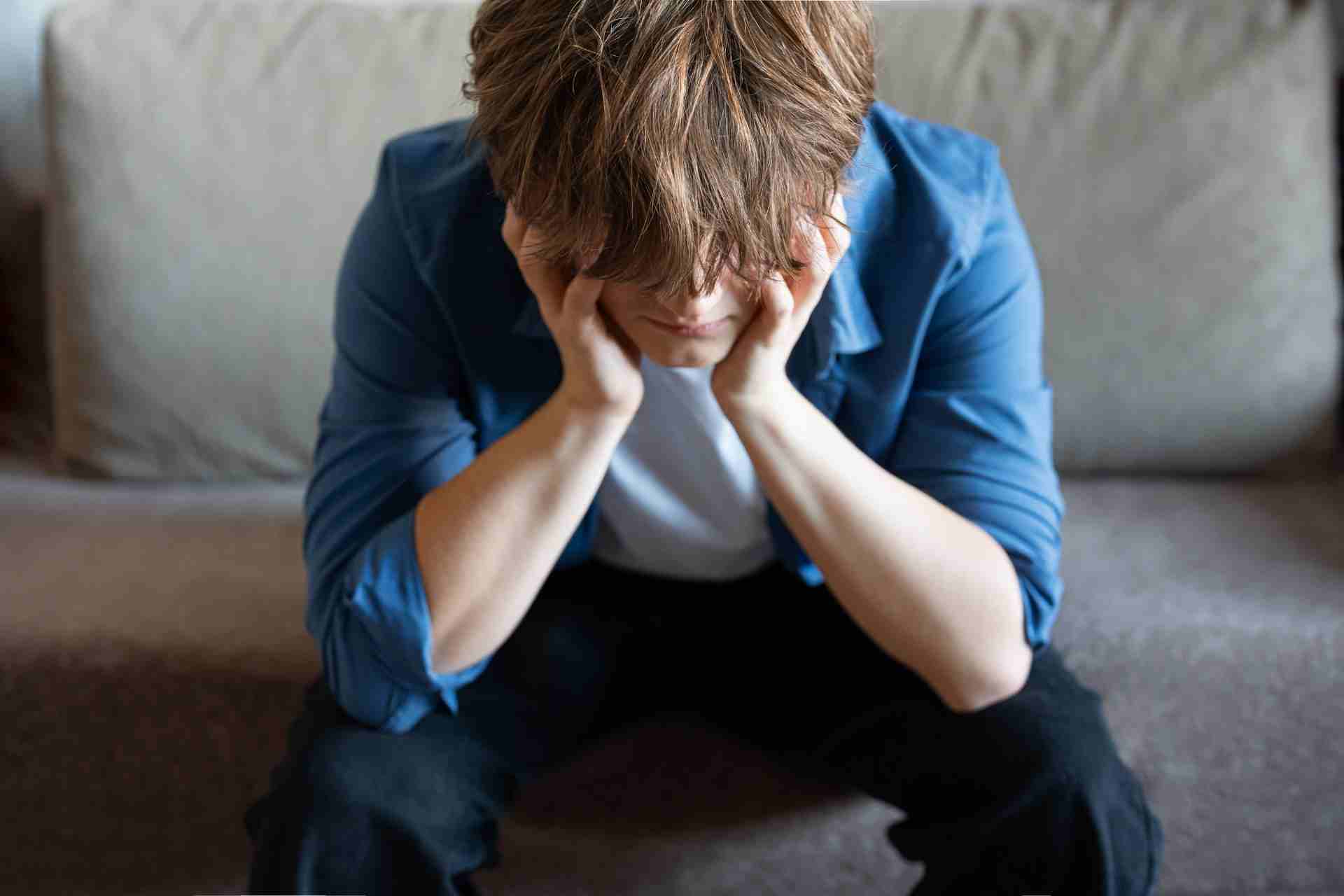 Teen sitting on a couch with head down, showing signs of mental health burnout, emotional exhaustion, and distress.