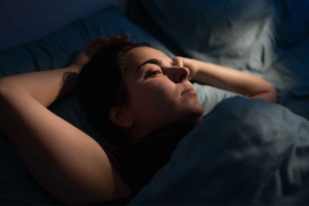 Woman lying awake in bed at night while experiencing anxiety and stress.