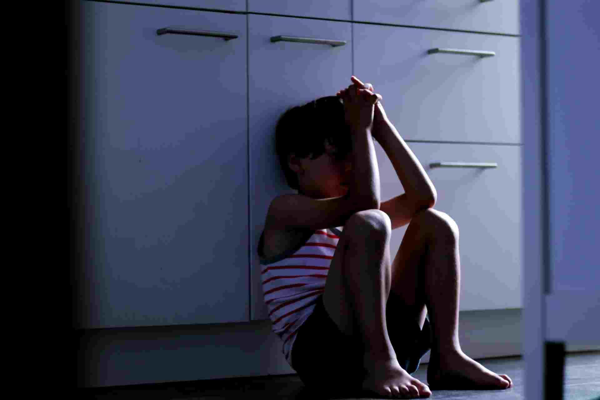Child sitting on the floor showing signs of emotional distress related to childhood trauma.