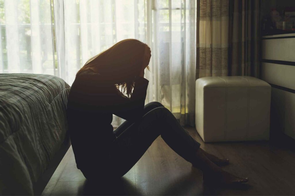 Woman sitting alone in a bedroom while experiencing symptoms of depression.